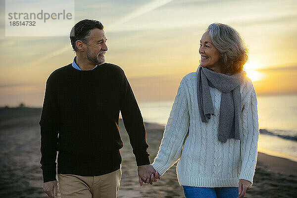 happy mature couple holding hands and walking at beach
