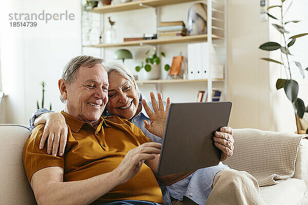 Glückliches älteres Paar gestikuliert bei einem Videoanruf über einen Tablet-PC zu Hause