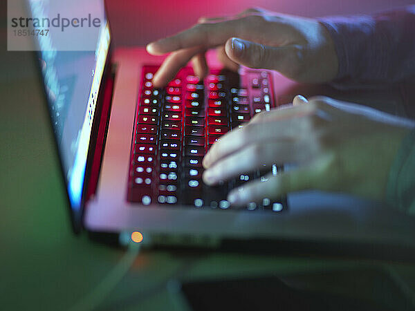 Hacker tippt im Büro auf beleuchteter Laptop-Tastatur
