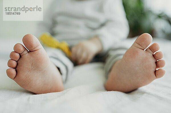 Barefoot feet of toddler boy sitting on bed