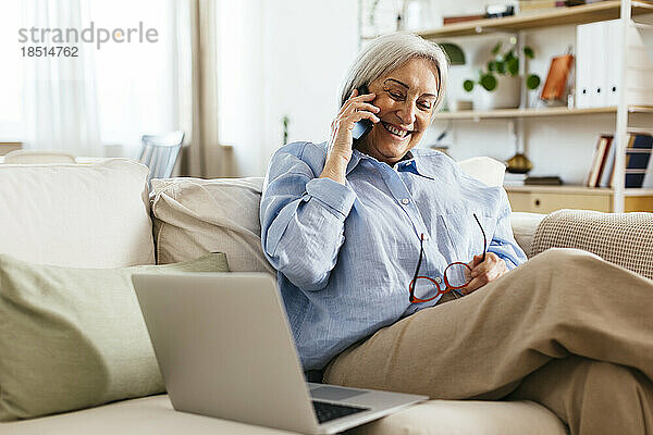 Glückliche ältere Frau  die zu Hause über ihr Mobiltelefon telefoniert