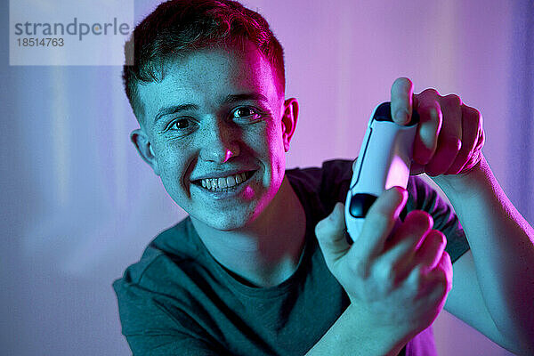 Happy young man playing video game in front of wall