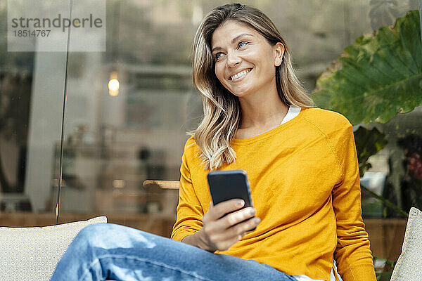 Glückliche Frau mit Smartphone sitzt im Café