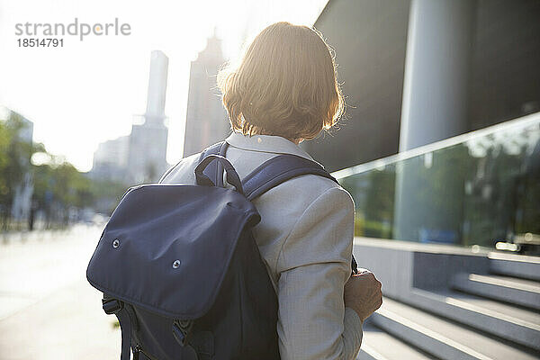 Geschäftsfrau mit braunen Haaren trägt an einem sonnigen Tag einen Rucksack