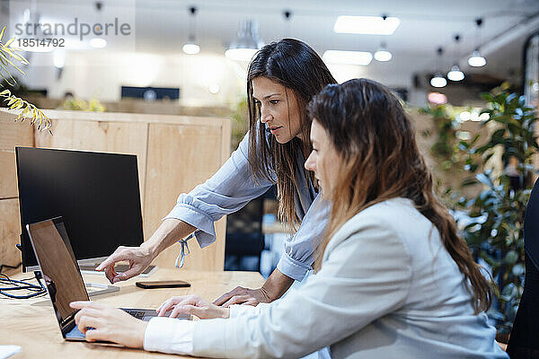 Geschäftsfrau und Kollegin diskutieren am Laptop im Büro