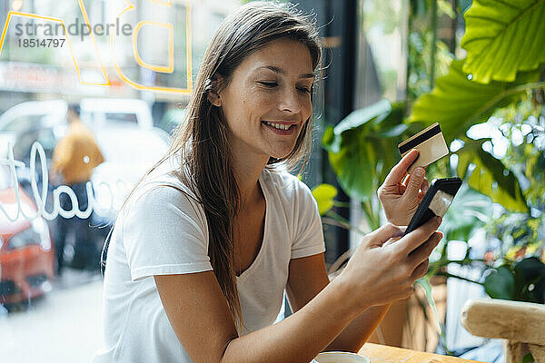 Lächelnde Frau mit Kreditkarte und Smartphone im Café