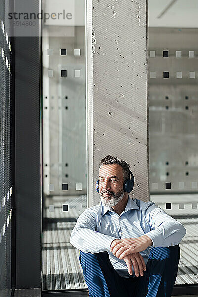 Nachdenklicher Geschäftsmann  der im Büro Musik über drahtlose Kopfhörer hört