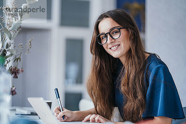 Lächelnde Geschäftsfrau sitzt am Schreibtisch mit Laptop im Büro