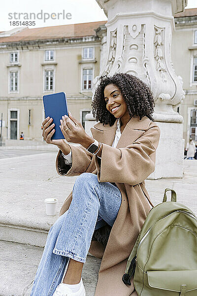 Glückliche junge Frau  die auf einer Treppe sitzt und ein Selfie mit einem Tablet-PC macht
