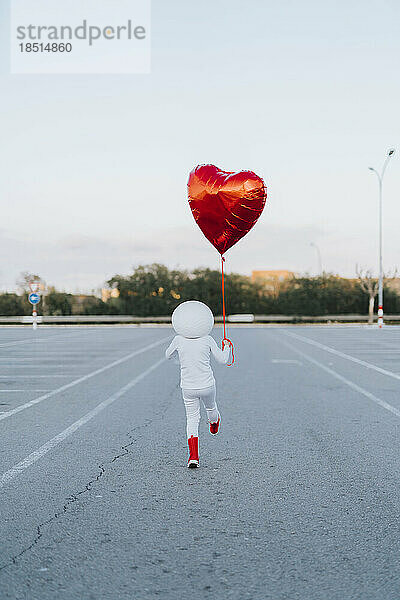 Als Astronaut verkleidetes Mädchen  das Spaß mit einem herzförmigen Ballon auf dem Parkplatz hat