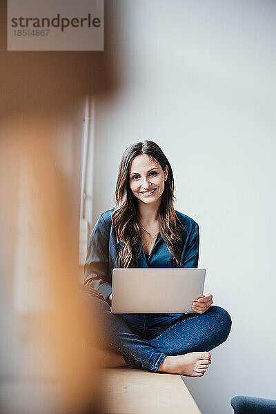 Glückliche Geschäftsfrau sitzt mit Laptop im Heimbüro