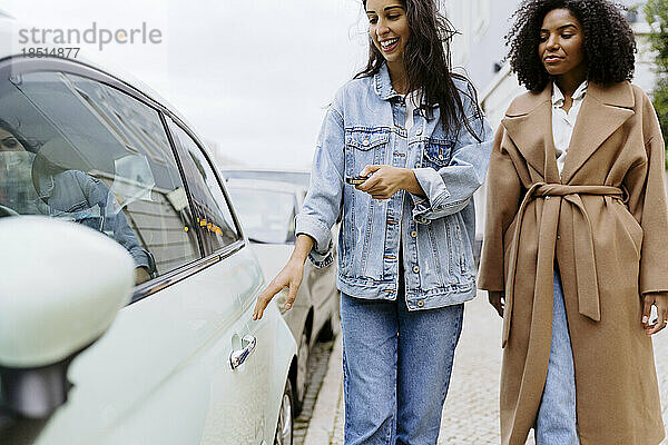Glückliche junge Frau mit Freundin  die Auto mit Funkschlüssel aufschließt