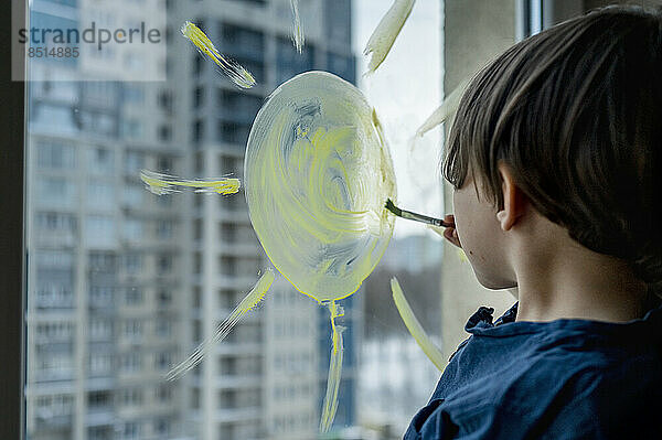 Boy drawing sun on glass with paint brush