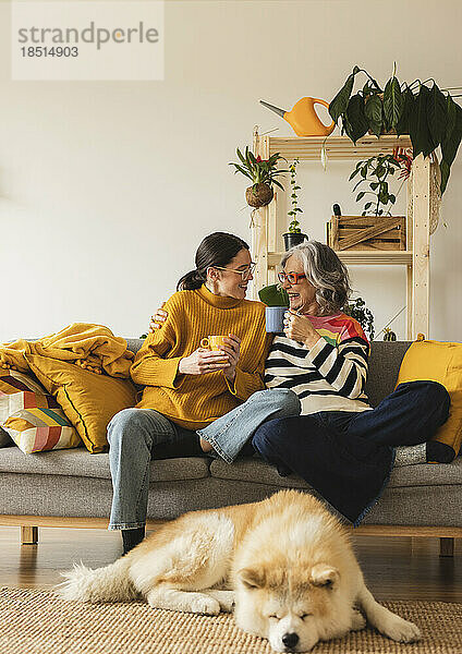 Lächelnde Mutter und Tochter mit Kaffeetasse verbringen gemeinsam ihre Freizeit zu Hause