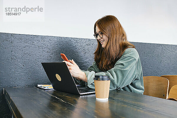 Lächelnder junger Freiberufler nutzt Smartphone im Café