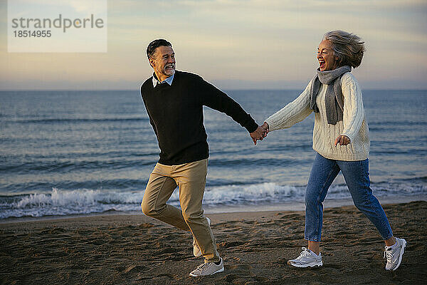 Glückliches älteres Paar hält Händchen und läuft am Strand