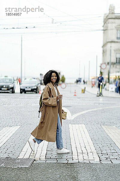 Lächelnde junge Frau überquert die Straße in der Stadt