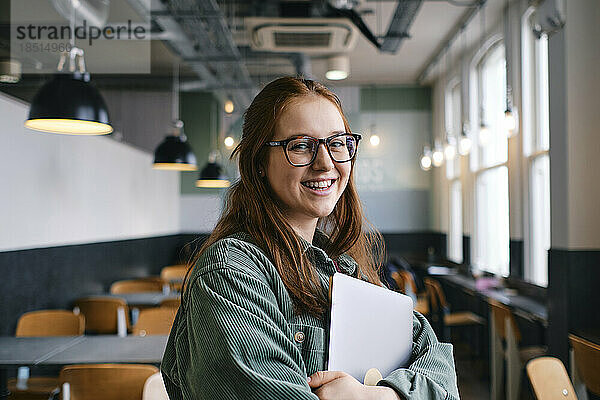 Lächelnder junger Freiberufler steht mit Laptop im Café