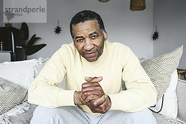 Mature man with hands clasped sitting on sofa at home