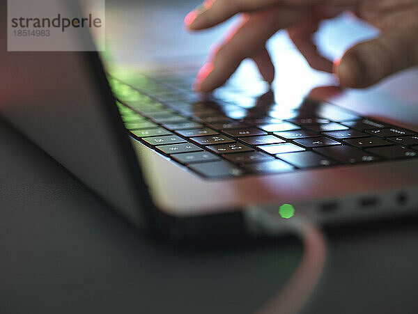 Hände tippen auf beleuchteter Laptop-Tastatur im Dunkeln im Heimbüro