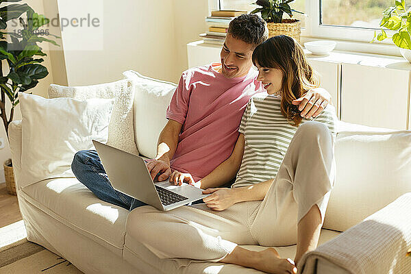 Lächelndes Paar benutzt Laptop und sitzt zu Hause auf dem Sofa