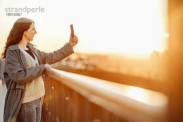 Glückliche Frau  die bei Sonnenuntergang ein Selfie auf einer Brücke macht