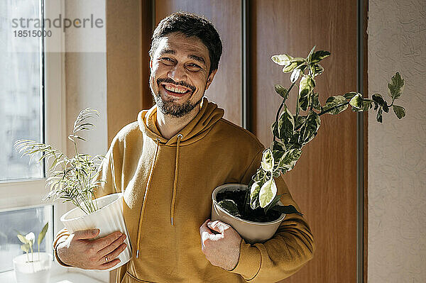 Happy man holding potted plants at home