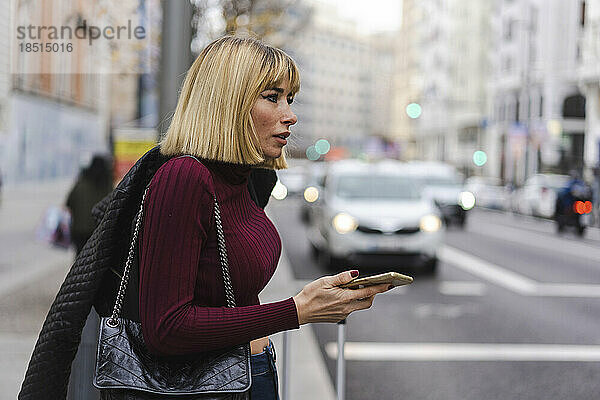 Frau hält Smartphone in der Hand und wartet auf Bürgersteig