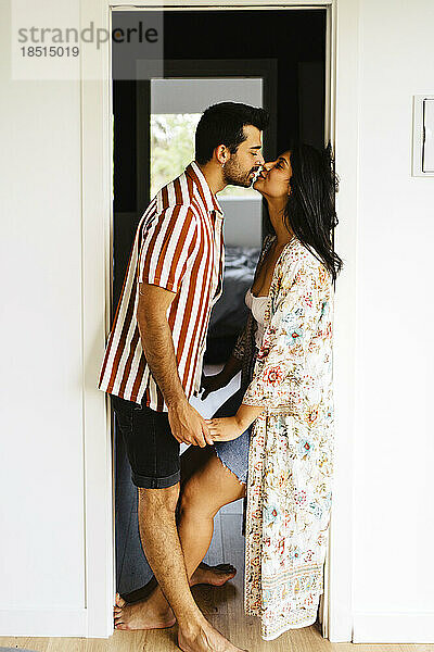Romantic couple kissing in doorway at home