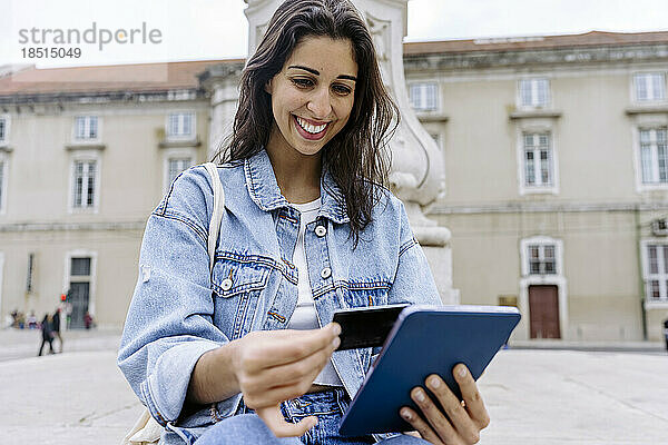 Glückliche junge Frau  die per Kreditkarte auf einem Tablet-PC bezahlt