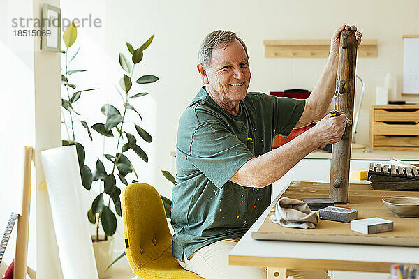 Lächelnder älterer Mann  der in der Werkstatt Holz bemalt