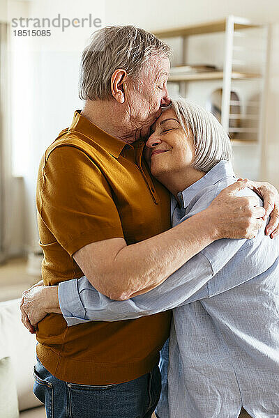 Älterer Mann küsst Frau zu Hause auf die Stirn