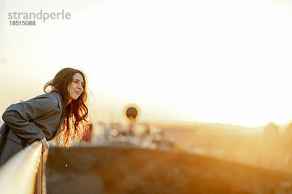 Lächelnde Frau lehnt bei Sonnenuntergang am Geländer