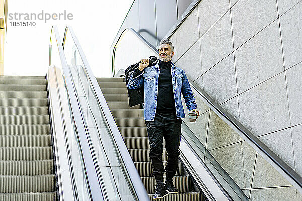 Lächelnder reifer Mann mit Tasche steht auf Rolltreppe