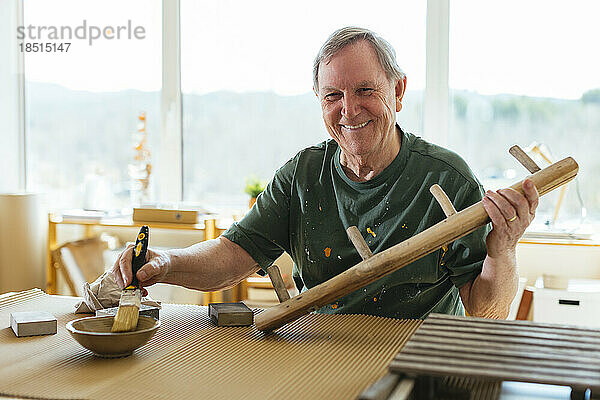 Lächelnder älterer Mann  der in der Werkstatt Holz bearbeitet