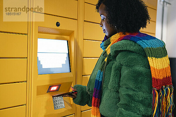 Frau bezahlt per Smartphone am Fahrkartenautomaten