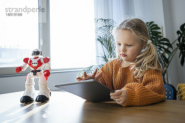 Mädchen benutzt Tablet-PC mit Roboter auf dem Tisch zu Hause