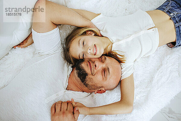 Smiling girl lying down with father on bed at home