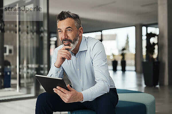 Nachdenklicher Geschäftsmann sitzt mit Tablet-PC im Büro