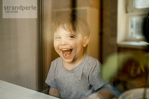 Cheerful cute boy seen through glass window