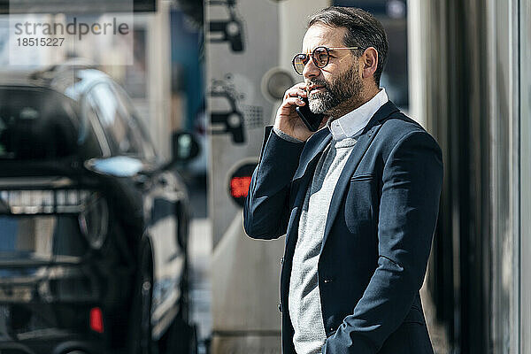 Geschäftsmann spricht am Smartphone und steht in der Autowaschanlage