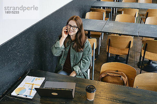 Lächelnder junger Freiberufler  der im Café mit dem Smartphone spricht