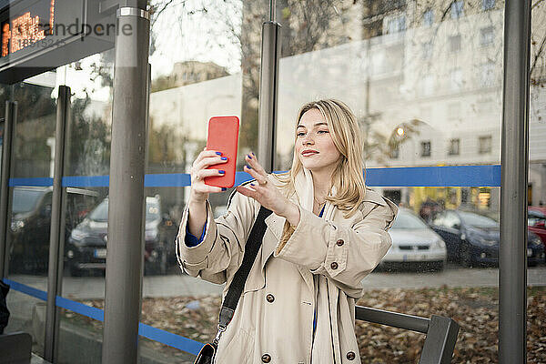 Junge Frau macht Selfie mit Smartphone an Bushaltestelle