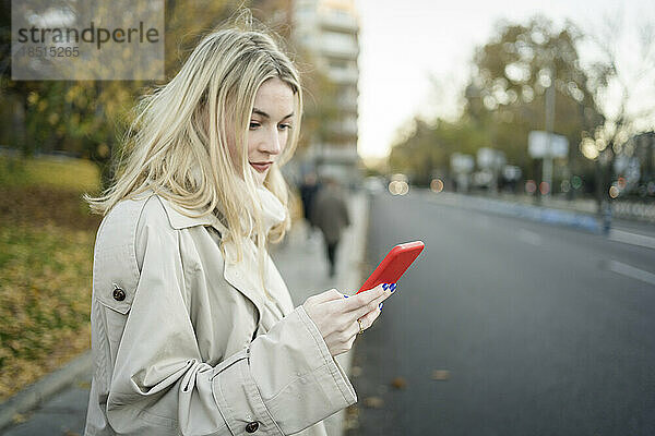 Blonde Frau benutzt Smartphone am Bürgersteig