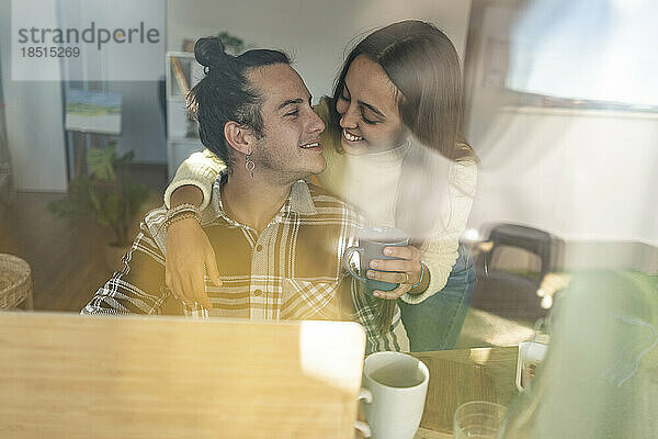 Affectionate couple embracing at home seen through glass