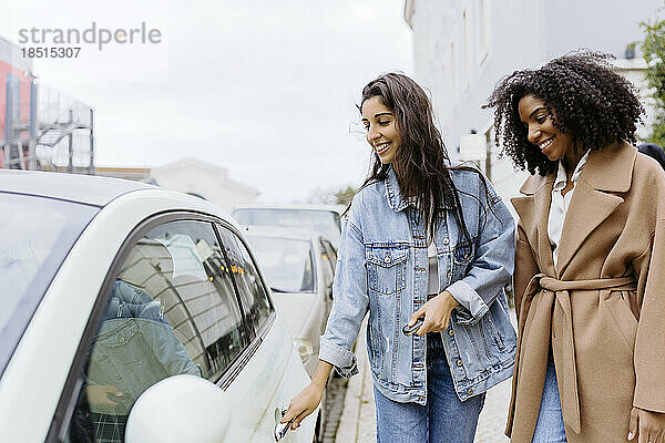 Lächelnde junge Frau mit Freund  der Auto mit Funkschlüssel aufschließt