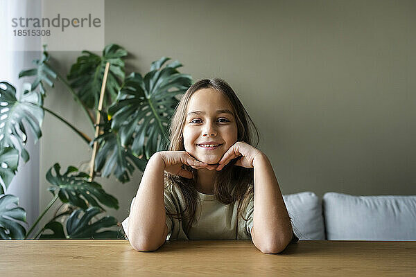 Smiling girl leaning on elbows at table in home