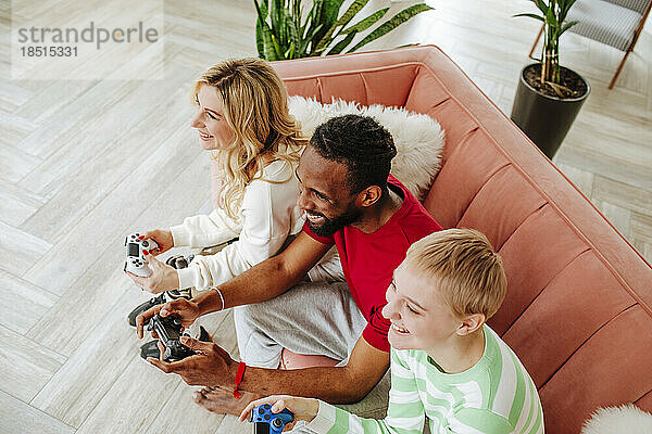 Friends with game controller playing video game sitting on sofa at home