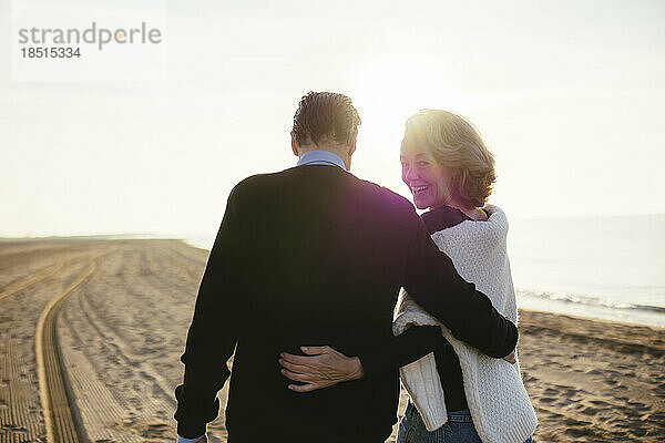 Lächelnde reife Frau mit Mann  der am Strand spaziert