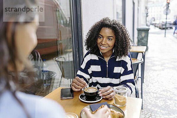 Lächelnde junge Frau sitzt mit einer Freundin im Straßencafé